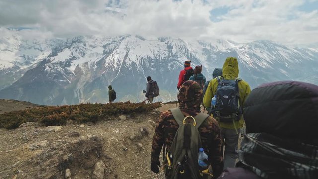 Tourist expedition trekking down in mountains next to giant snow massif in cloud