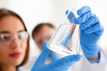 Female technician arms in protective gloves hold fluid sample bottle closeup. Medical worker in...