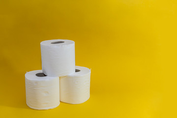 A stack of three white disposable toilet rolls on a yellow background. Soft fresh cotton. Essential...
