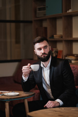 Portrait of a young handsome bearded man. A businessman in a suit sits at a table in a cafe or restaurant.