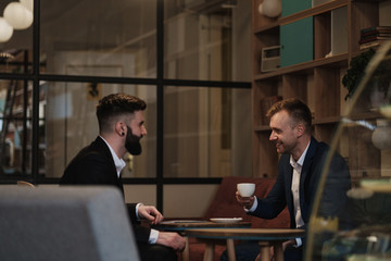 Two men in suits sit in a restaurant. A business meeting. Men drink coffee.