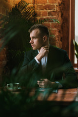 A handsome young bearded man blond in a suit and shirt in a restaurant with a loft interior. He sits at a table, read a magazine.