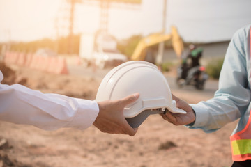 Foreman giving hard hat to partner for use hard hat to protect in building construction site