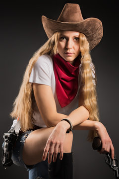 Studio portrait of a girl in a cowboy hat, with a red bandana, and a gun in her hand
