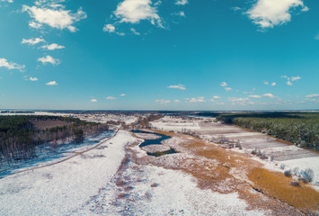 View from above of the countryside and brook on a sunny day. Snowy nature landscape with blue sky. Early spring