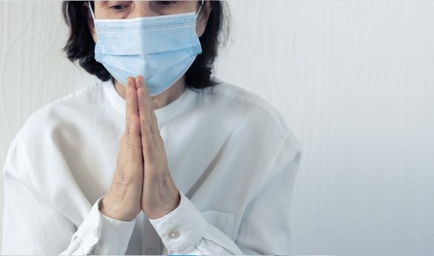 Coronavirus quarantine and Air pollution pm2.5 concept. Old sick woman wearing blue respirator mask for protect and praying to god. Wuhan, China epidemic virus symptoms background.