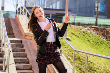 Spring vertical photo of a happy smiling beautiful girl with emotions in the sun outdoors on the background of the steps in the city. Pretty model posing with hands on camera.