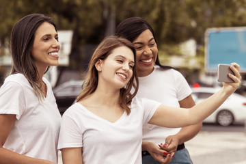 Smiling women posing for selfie on street. Cheerful young ladies taking selfie with smartphone. Concept of self portrait