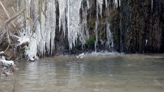Mały leśny wodospad nad śródlesnym cieku pokryty lodem powstałym po nocnych przymrozkach