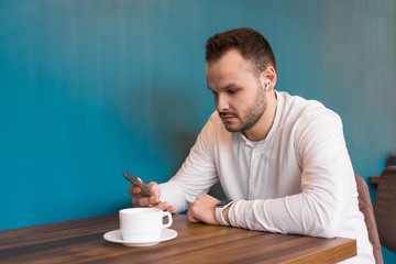 Young businessman in a white shirt looks at the phone and drinks coffee