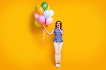 Full body photo of attractive funny lady hold many colorful air balloons birthday surprise event party wear polka-dot blue shirt white pants shoes isolated yellow color background