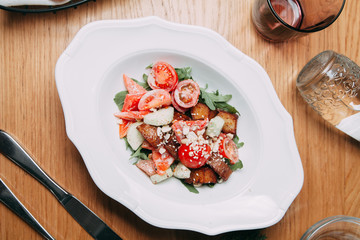 Restaurant serving salad with cheese, tomatoes and herbs. Fresh vegetable salad on a white plate.