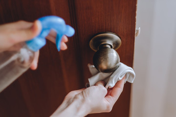 Woman cleans the door handle with an antibacterial spray