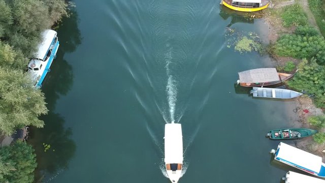 Aerial footage using a drone of a small boat leaving a ripple effect in the water which is a river.