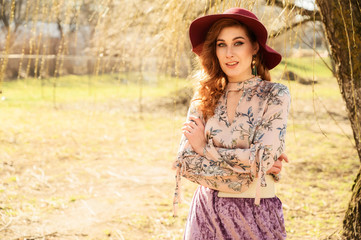 Photo of a fashionable glamorous Beautiful woman with long hair in a hat in a spring park in the sun. Model stands outdoors