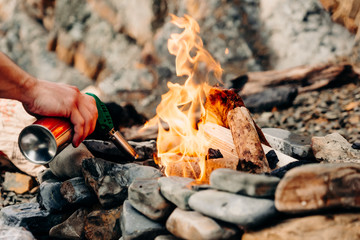 Man with a butane can burner kindles a fire in a bonfire on a stone beach