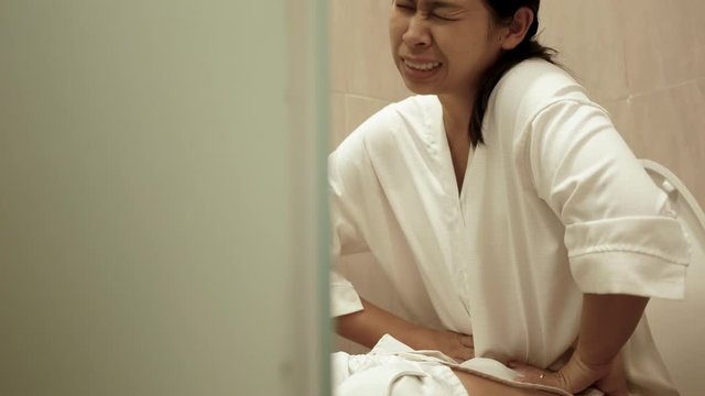 Young Asian woman suffering from constipation on toilet bowl at home. Health care concept.