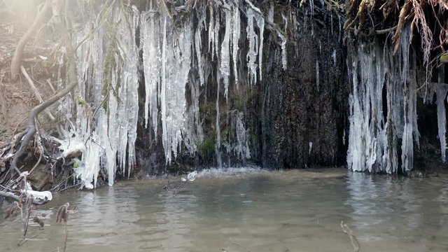 Mały leśny wodospad nad śródlesnym cieku pokryty lodem powstałym po nocnych przymrozkach