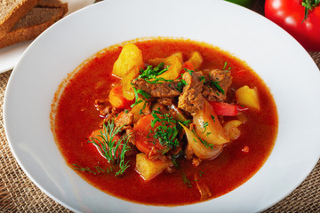 Hot beef hungarian  goulash soup with paprika, beef, potatoes, carrots, onion, pepper and herbs. Ingredients for dish.  Rustic background.