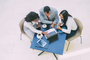Diverse team working on project during coffee break. Business man and women sitting at table with tablet and cups, using laptop. Teamwork concept. Top view
