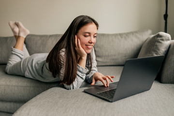 Attractive european young woman with long dark hair wearing pajamas working at home with laptop during quarantine