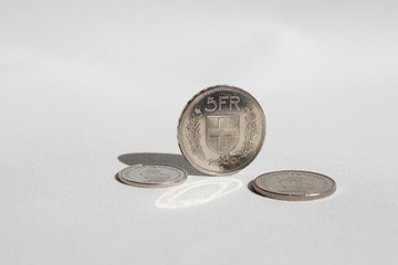 Swiss Franc coins, one, two and five, standing on a white background.