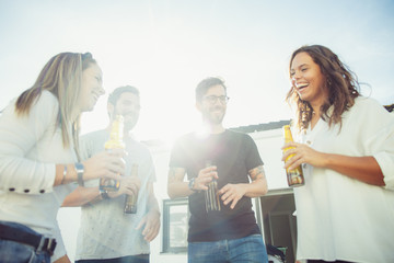 Cheerful carefree friends enjoying party, drinking beer, chatting on outdoor terrace. Young men and...
