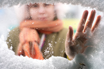 Girl hand cleans snow from the frozen glass of a car.  View from inside of car.