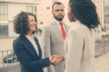 Consultant and customers meeting outside. Business man and women standing near city building and shaking hands. Diverse partners concept