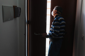 Man with a mask confined in quarantine to prevent coronavirus spread to the door.