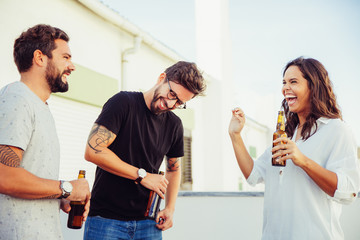 Excited happy friends drinking beer, chatting and laughing on outdoor terrace. Young men and woman in casual meeting outside. Old friends meeting or fun concept