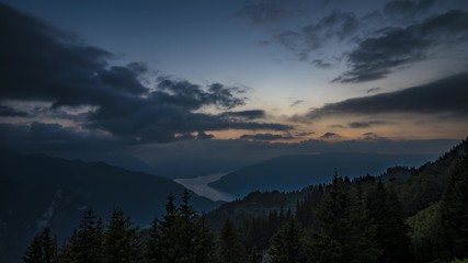 Fototapeta na wymiar Dark forest after sunset with clouds and lake in background. Switzerland