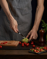 Chef man hands on cook  appetizer sandwiches with guacamole and tomatoes. healthy breakfast food, vegetarian food, diet. Gark style photo.