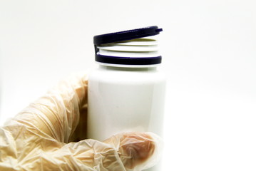 the doctor's gloved hand holds a jar of medicine