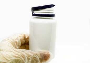 the doctor's gloved hand holds a jar of medicine