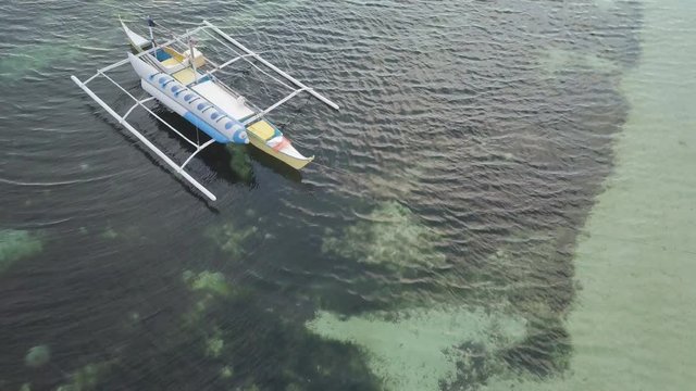 4K Top down aerial shot: flying low above a small bangka (typical filipino boat) over the crystal water of a paradise beach in Southeast Asia (Siquijor Island, The Philippines)