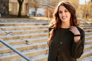 Fototapeta premium Portrait of a pretty fashionable brunette woman with long beautiful hair in a suit on the background of the steps of the building in sunny weather