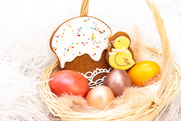 Easter holiday. Colored eggs in a basket. Easter gingerbread chicken and Easter cake. on a light background.