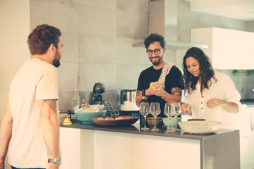 Happy couple cooking dinner for friends together in kitchen. Young men and women in casual meeting indoors. Cooking at home concept