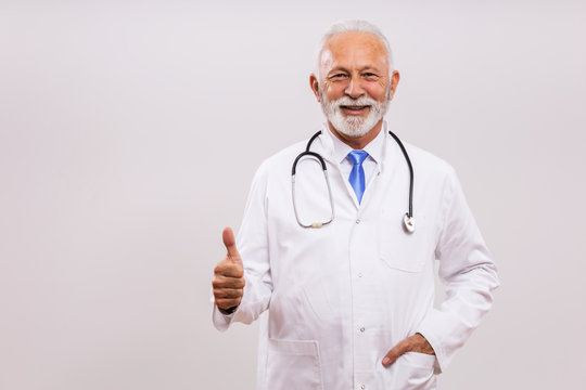 Portrait Of Senior Doctor Showing Thumb Up On Gray Background.