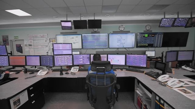 A worker sits in front of many monitors. Production room. Monitoring of technical processes in oil production.