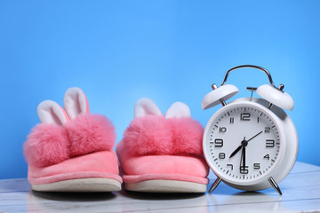 Pink girl slippers with white retro alarm clock on a wooden floor and blue background