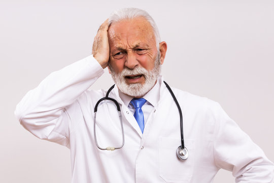Image of tired senior doctor having headache on gray background.