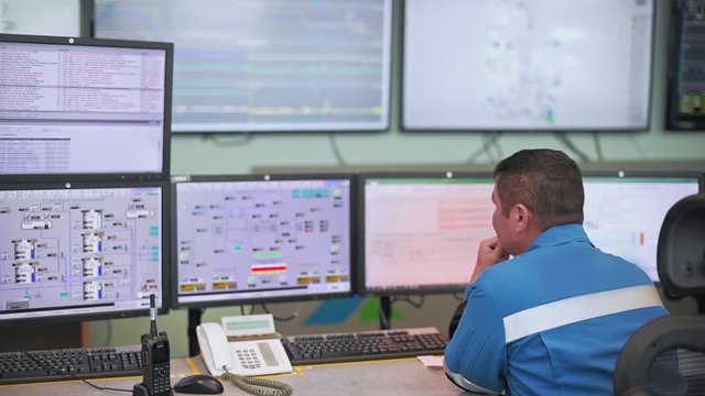 A worker sits in front of many monitors. Production room. Monitoring of technical processes in oil production. Instruments for monitoring indicators in the manufactory. Remote control.