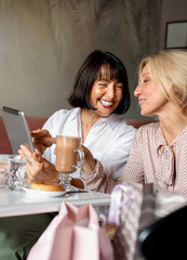 Two mature women chatting and using the tablet device while having lunch in cafe