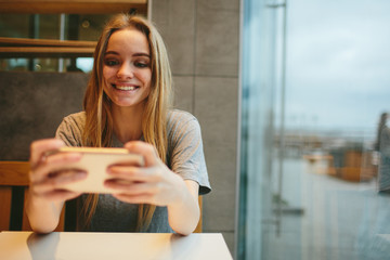 Fototapeta premium The blonde uses the phone. Girl and smartphone. A woman is sitting in a cafe with a cellular