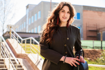 Photo of a pretty fashionable brunette woman with long beautiful hair with a smile in a suit on the background of the steps of the building in sunny weather