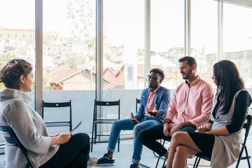 Diverse startup team consulting coach. Group of young men and women sitting in training room, talking, discussing work issues . Business training concept