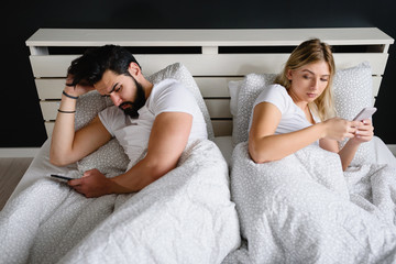 Fototapeta na wymiar Young adult couple using smartphones in the bed addicted to social networking. Mobile addiction concept. Jealous wife.