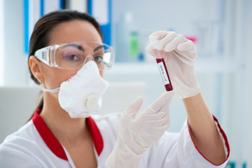 Woman doctor in a mask with a flask with a blood sample. Laboratory research and Covid-19...